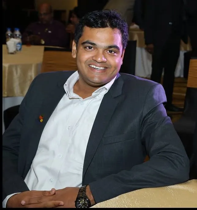 Vimal Hari smiling in a red plaid shirt and tortoise shell glasses